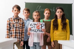 Two boys and three girls standing in front of a chalk board holding a sign that says "Stop Bullying".